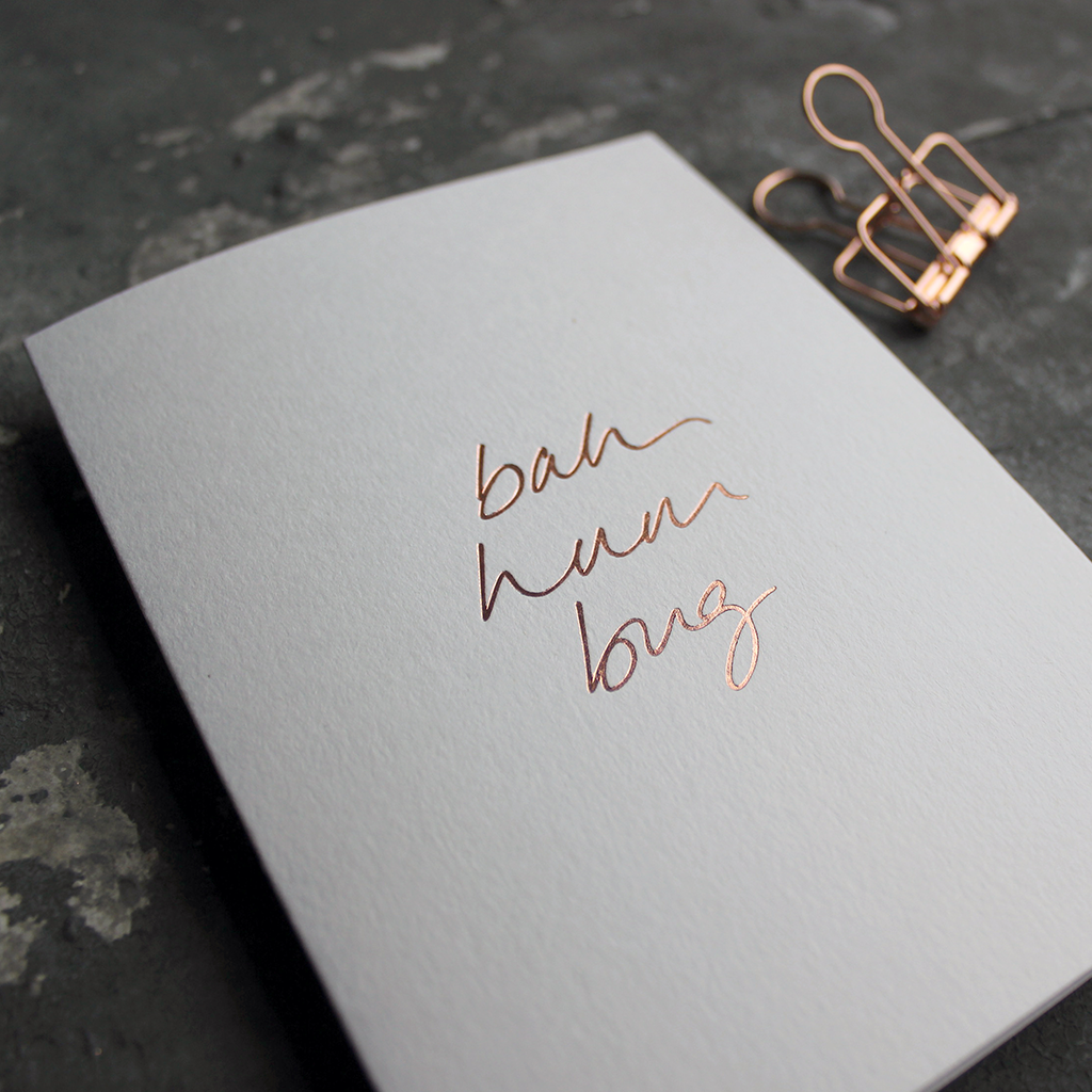 This white christmas card has 'Bah Hum Bug' handprinted in rose gold foil in handwriting on the front.