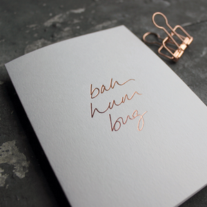 This white christmas card has 'Bah Hum Bug' handprinted in rose gold foil in handwriting on the front.