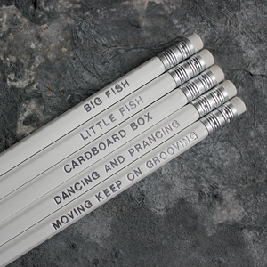 White HB pencils printed with silver foil phrases and packaged in a grey paper box. 