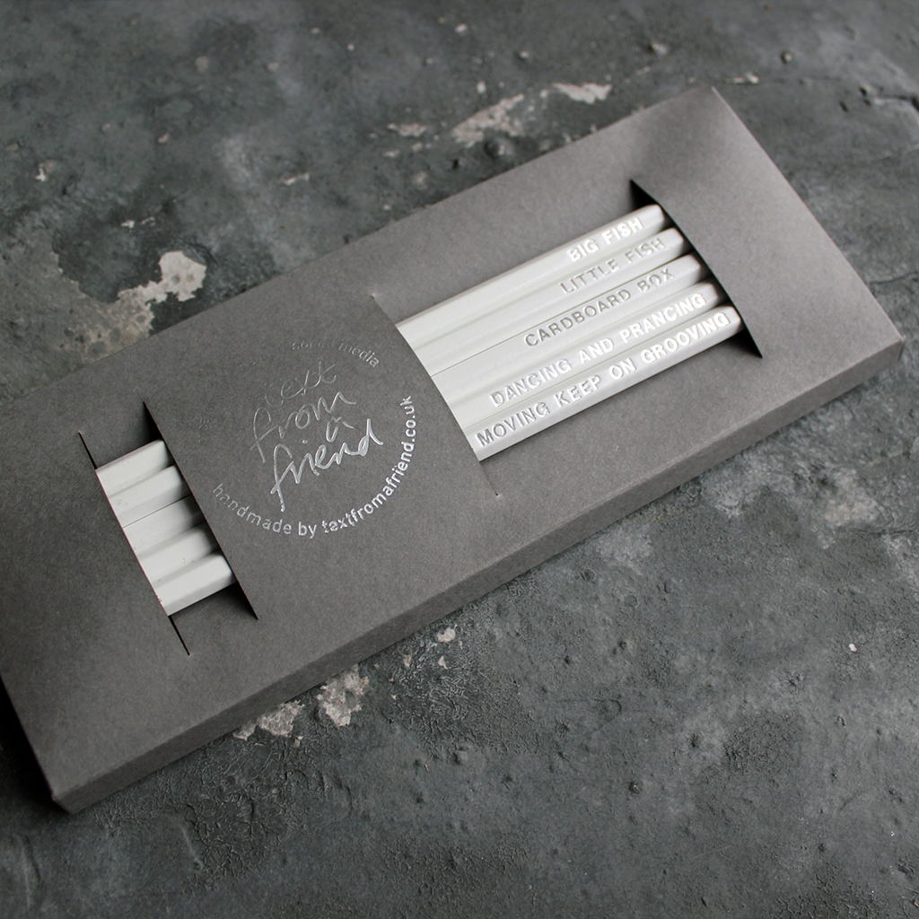 White HB pencils printed with silver foil phrases and packaged in a grey paper box. 