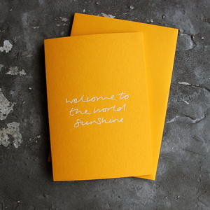 This yellow new baby card says Welcome To The World sunshine in white foil.