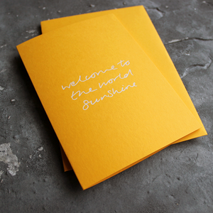 This yellow new baby card says Welcome To The World sunshine in white foil.