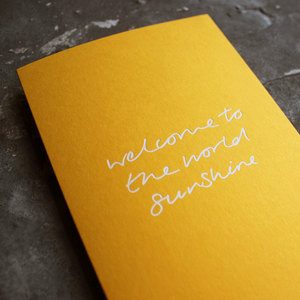 This yellow new baby card says Welcome To The World sunshine in white foil.