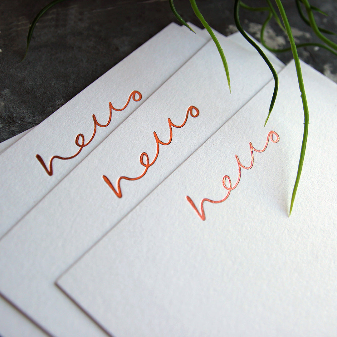 a close up shot of 3 luxury white notecards which are handfoiled in rose gold foil in handwriting and say hello