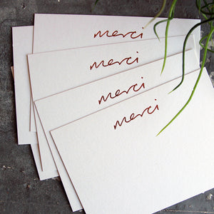 a group shot of luxury white notecards which are handfoiled in rose gold foil in handwriting and say merci