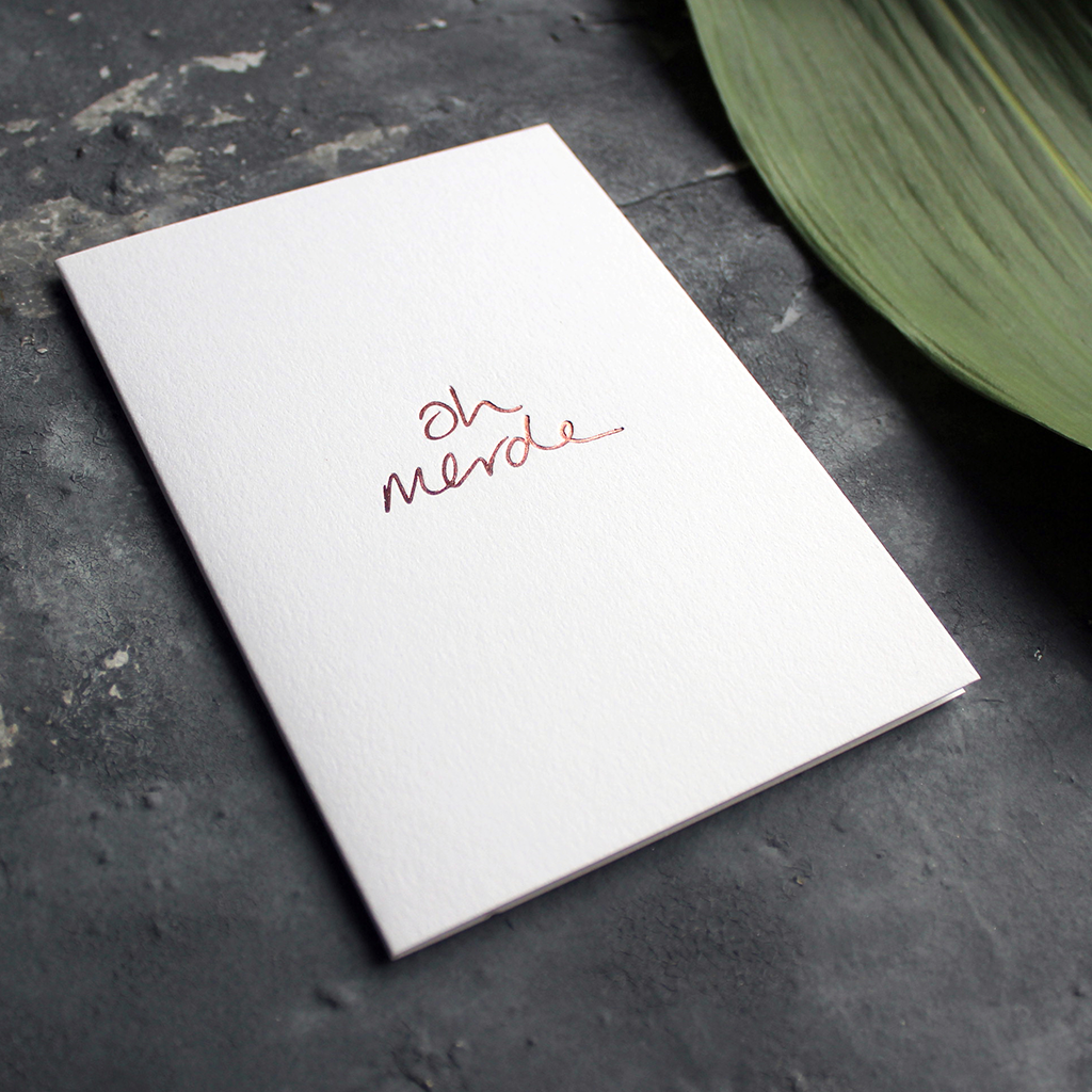 a luxury handwritten rose gold hand foiled message says Oh Merde on the front of the card