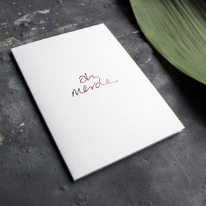 a luxury handwritten rose gold hand foiled message says Oh Merde on the front of the card