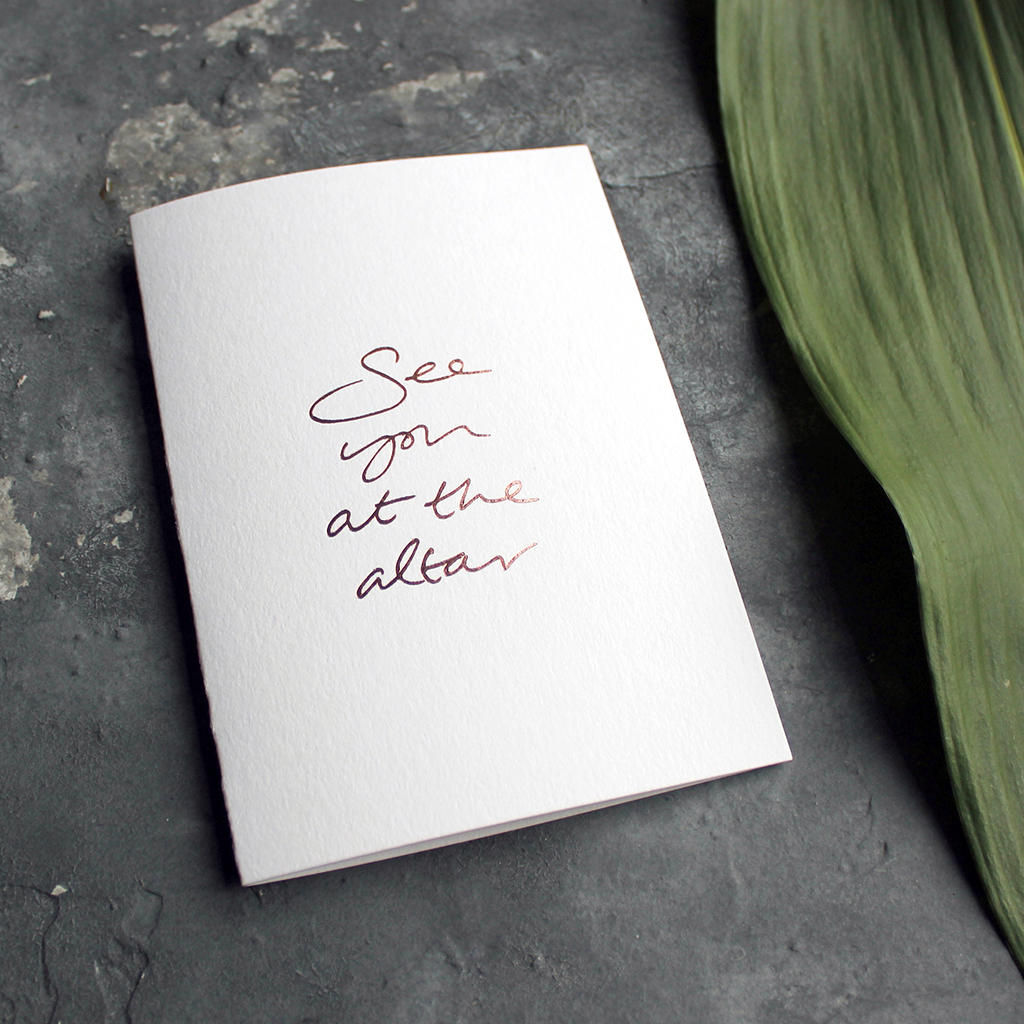 a luxury white wedding card that's handwritten with a rose gold foil message saying See You At The Altar