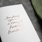 This luxury card will cheer the recipient up. It says Sending You A Ray of Fucking Sunshine on the front, handwritten and hand foiled in rose gold