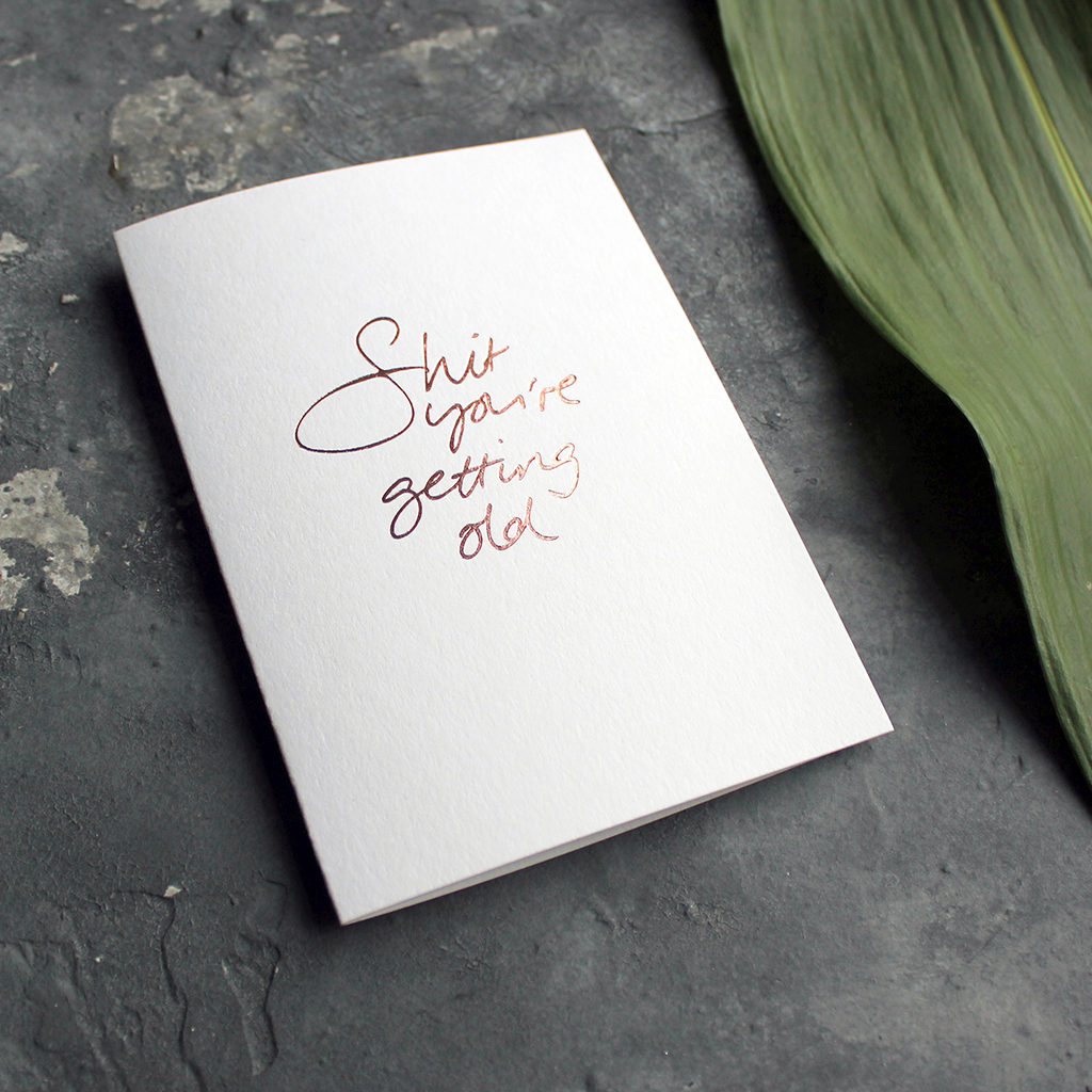 A birthday card with the message 'Shit you're getting old' hand written and hand foiled in rose gold