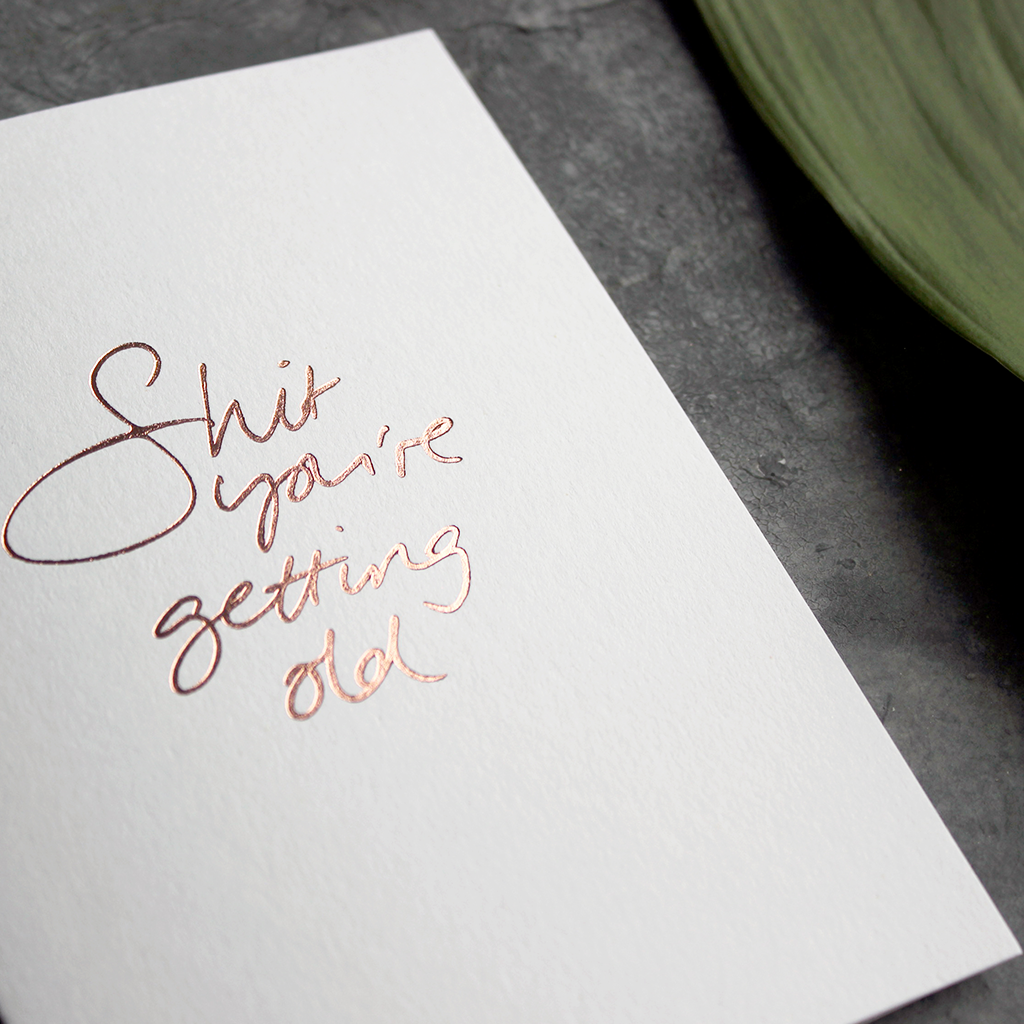 A birthday card with the message 'Shit you're getting old' hand written and hand foiled in rose gold
