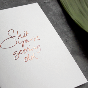 A birthday card with the message 'Shit you're getting old' hand written and hand foiled in rose gold