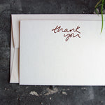 a luxury white notecard which is handfoiled in rose gold foil in handwriting and says thank you placed on top of a matching envelope