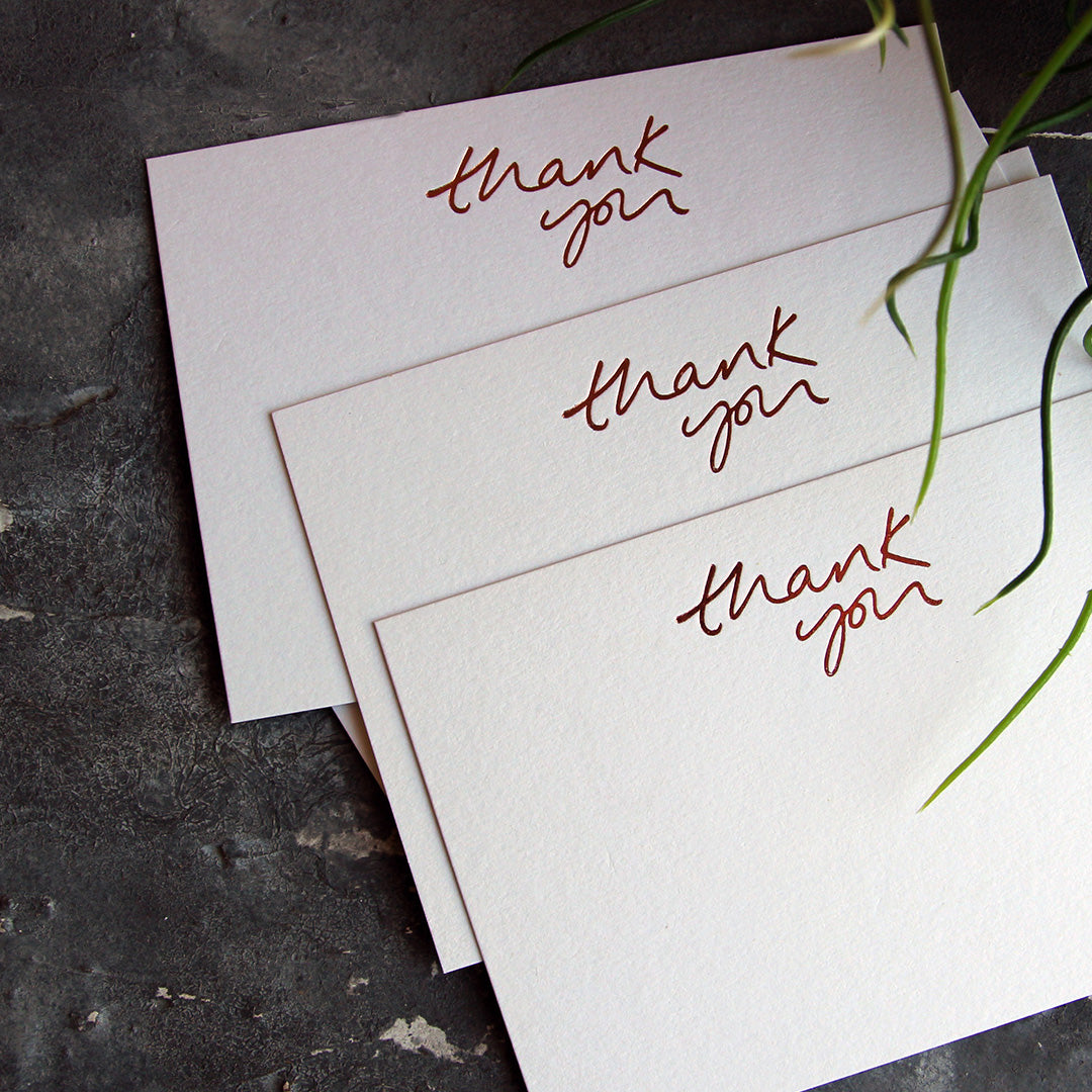 a group shot of luxury white notecards which are handfoiled in rose gold foil in handwriting and say thank you